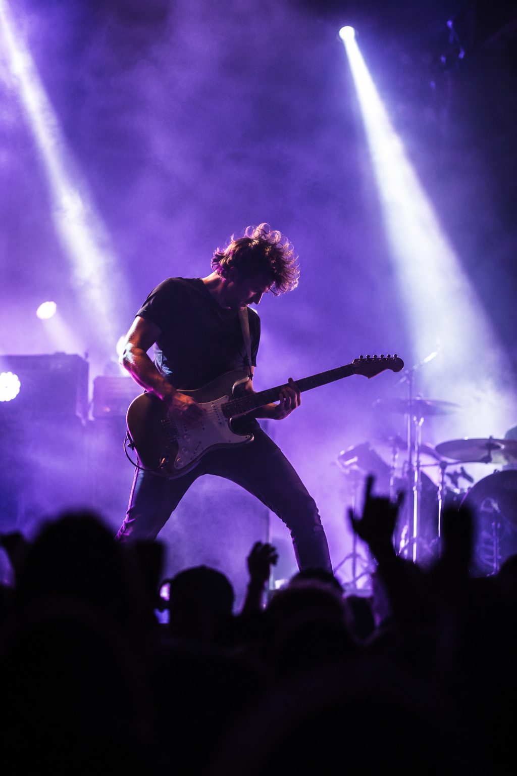 Electric guitarist on a dark stage, backlit by purple haze and narrow spotlight beams
