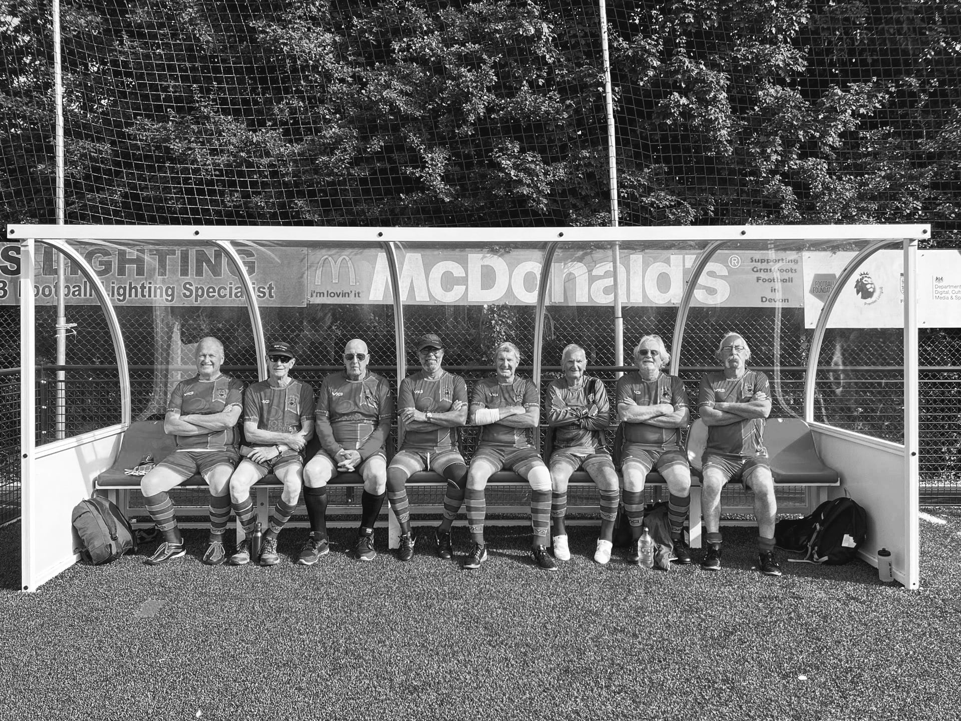 Old black-and-white team photo of local players seated together on the sideline after a match