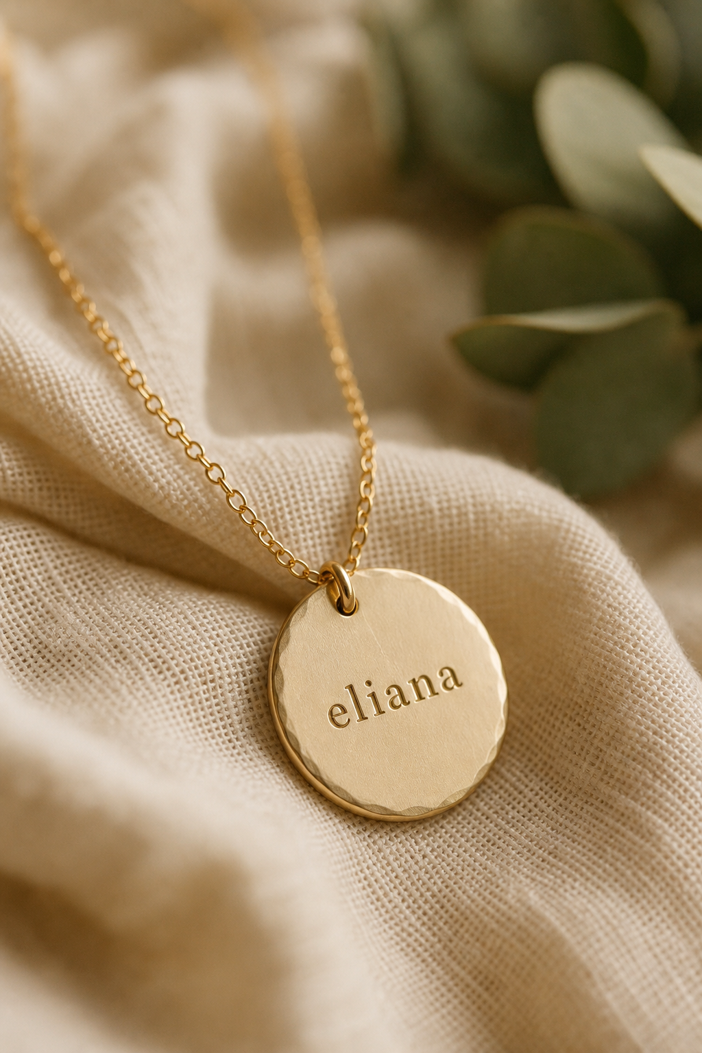 Macro photo of a hand-stamped gold necklace pendant engraved with a name, resting on soft linen fabric