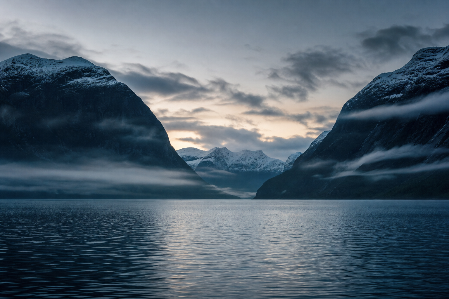 Panoramic Nordic fjord at dawn with cold blue water, dark mountain ridges, and soft mist