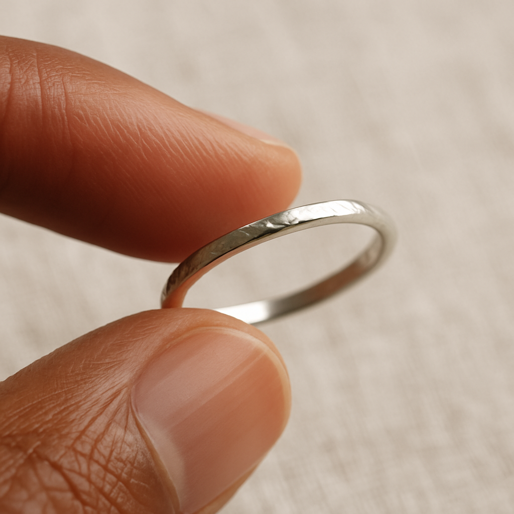 A hand holding a silver ring, revealing its delicate hand-finished texture