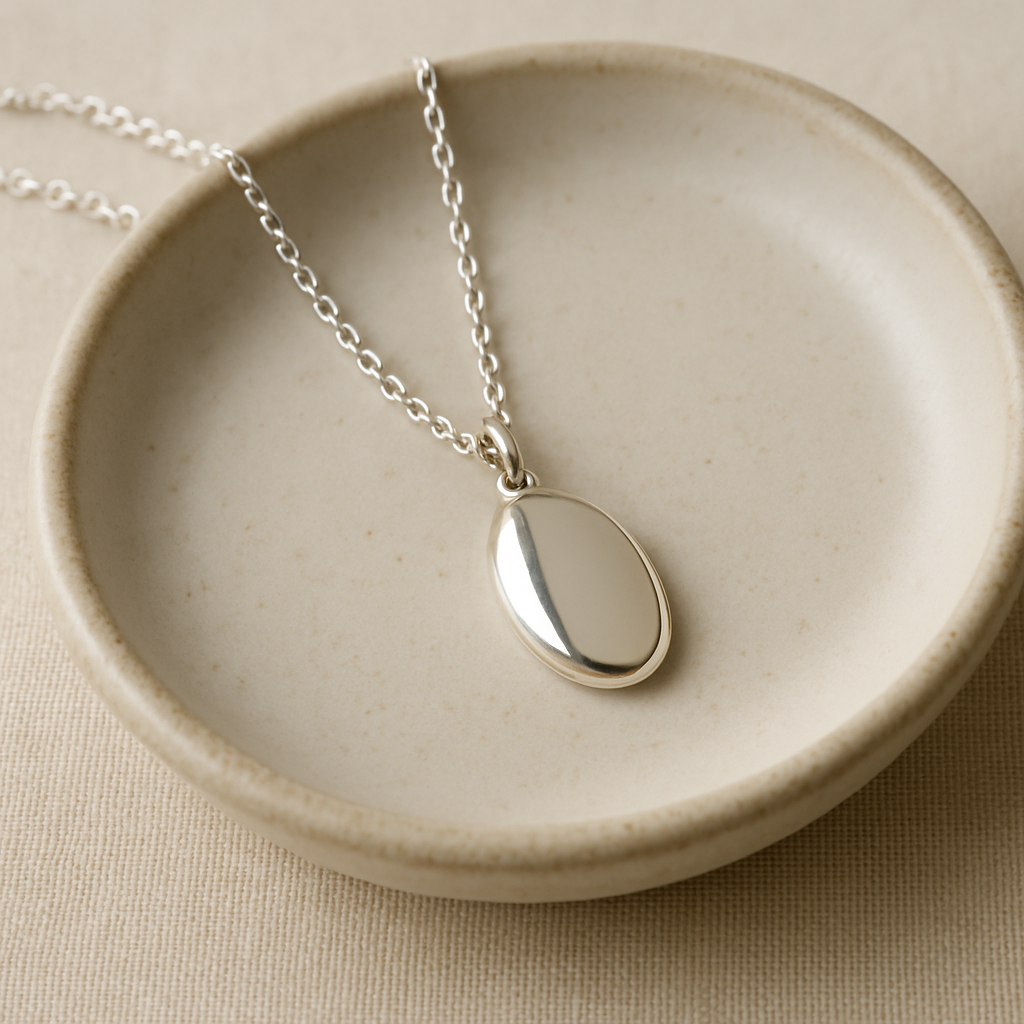 Fine silver chain with an oval pendant on a pale ceramic dish