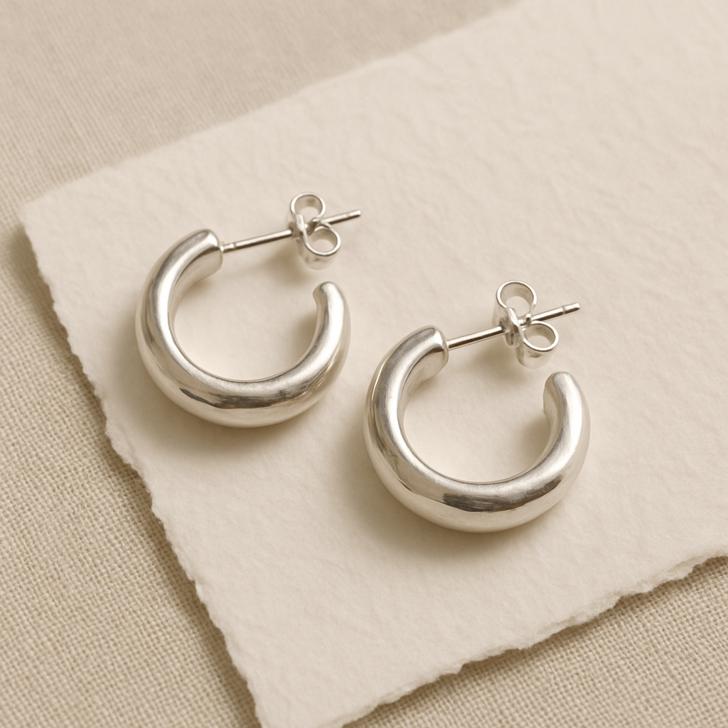 Small sculptural silver hoop earrings on textured handmade paper