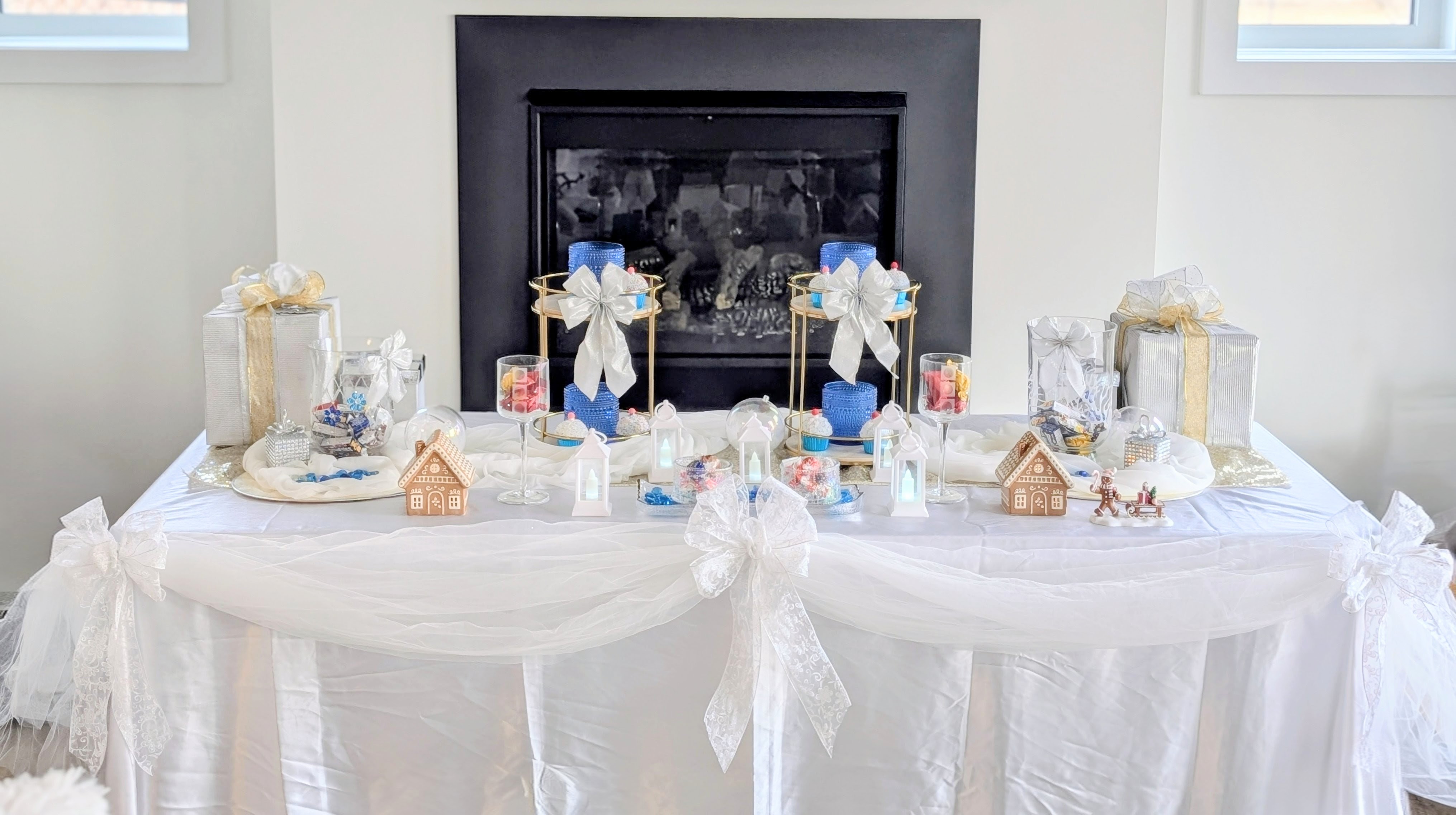 Bridal shower candy buffet table with pink bows, gold tiered stands, candles, and white tulle draping in front of a fireplace
