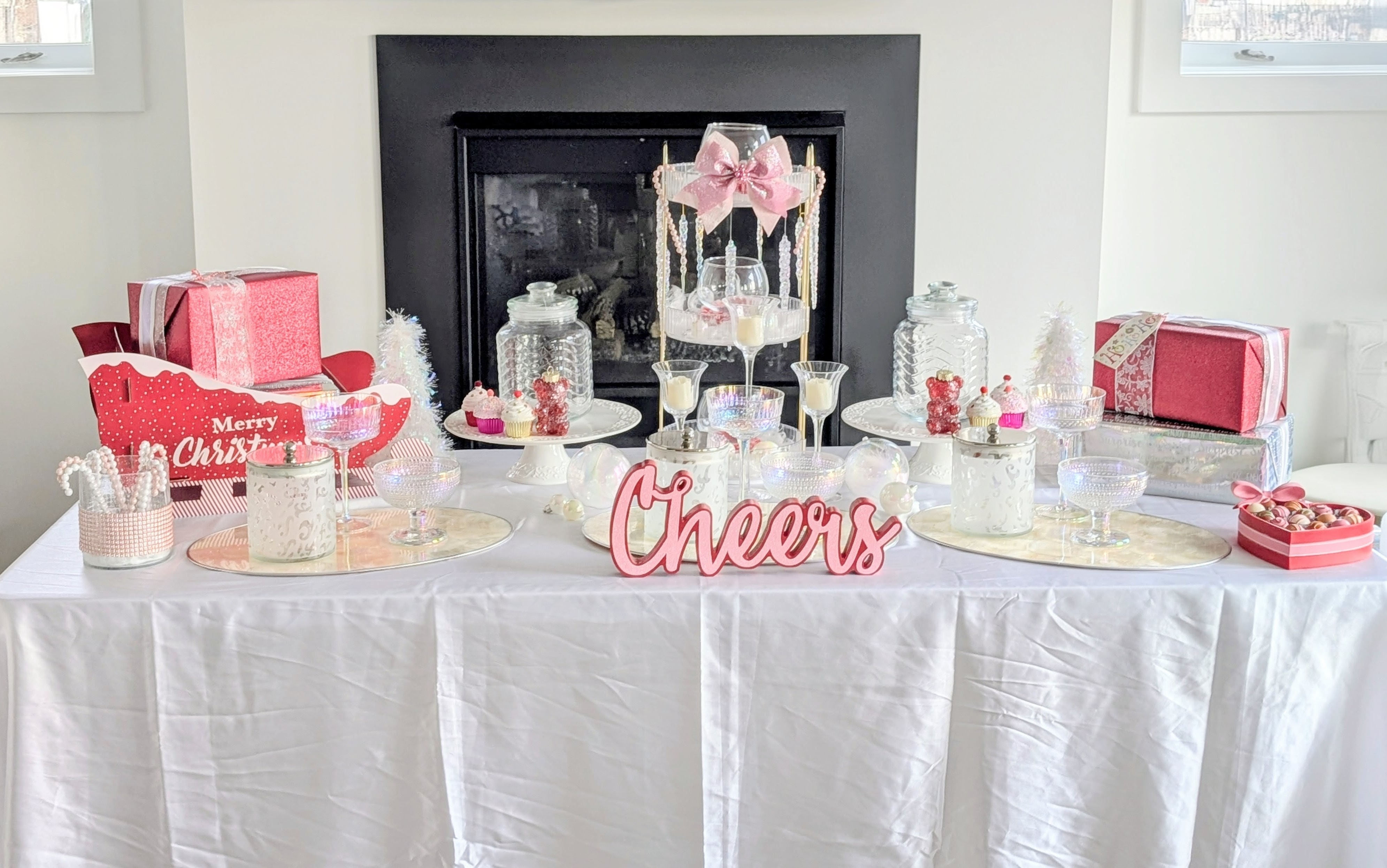 Valentine-themed candy table with pink ribbon decor, heart-shaped candy boxes, glass vessels, and a centerpiece sign reading Cheers