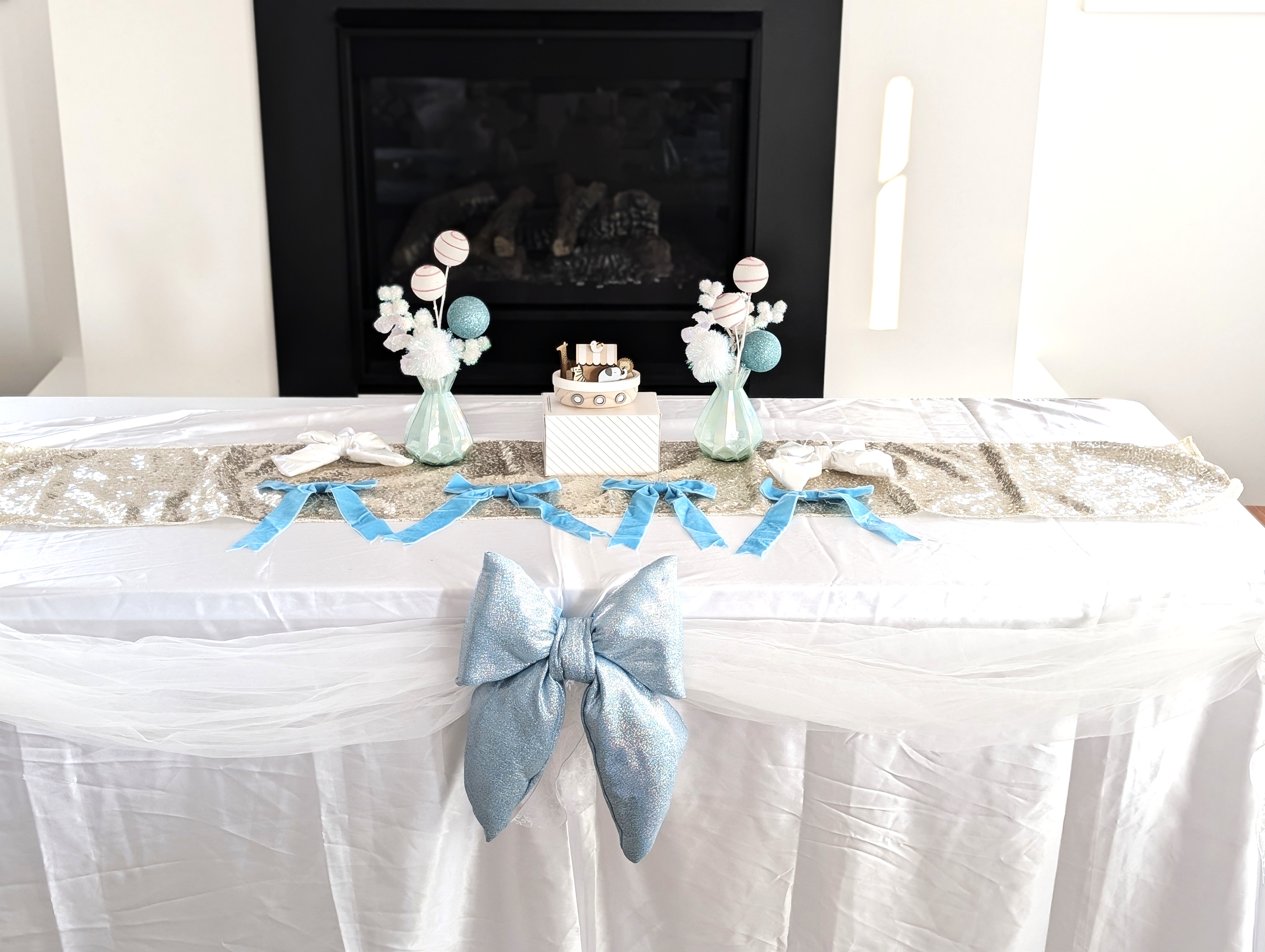 Baby shower dessert display with glittering blue bow centerpiece, silver runner, and pastel blue decorative elements