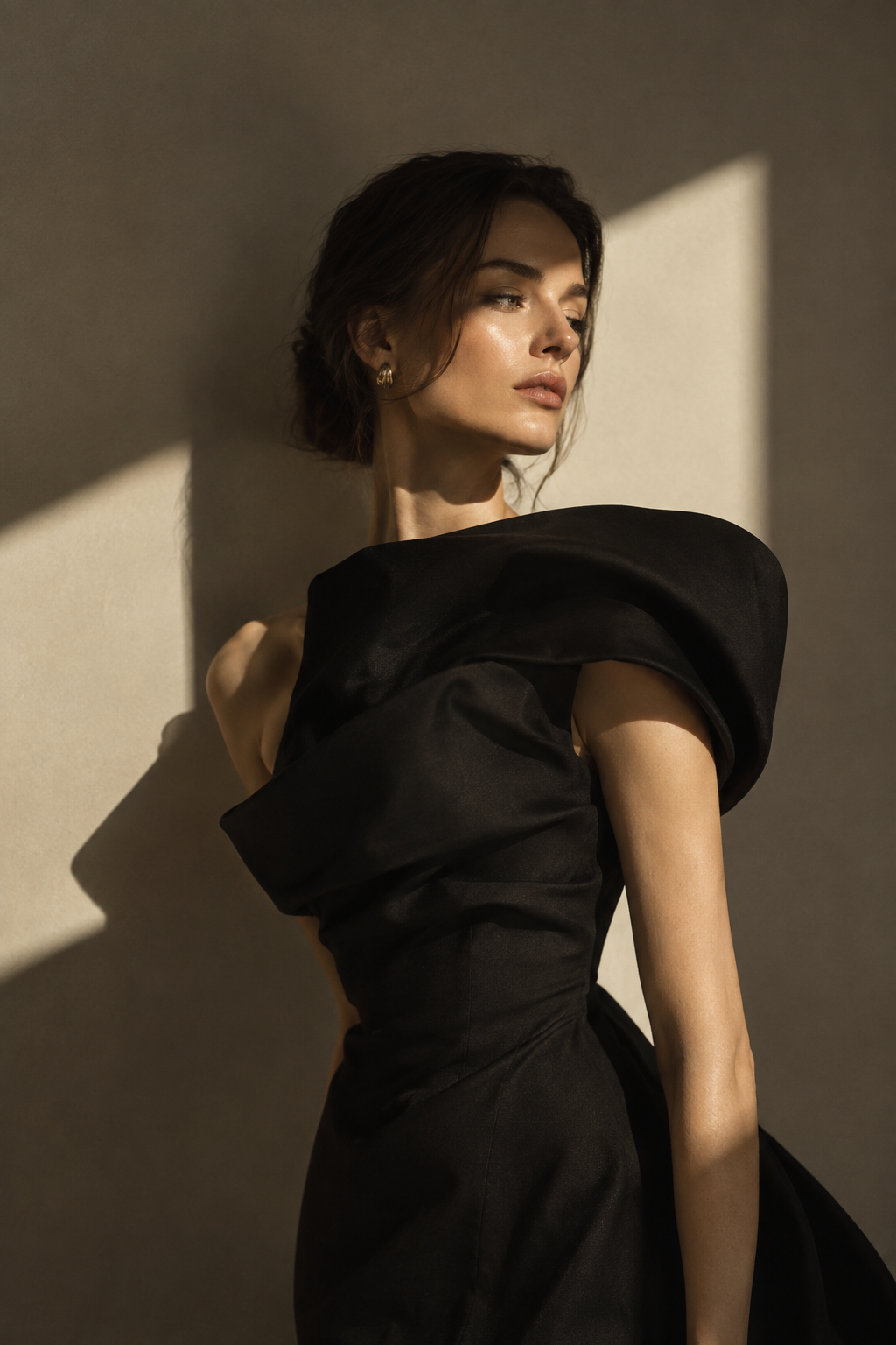 Refined fashion portrait with sculptural shadows cast across a model in a black dress