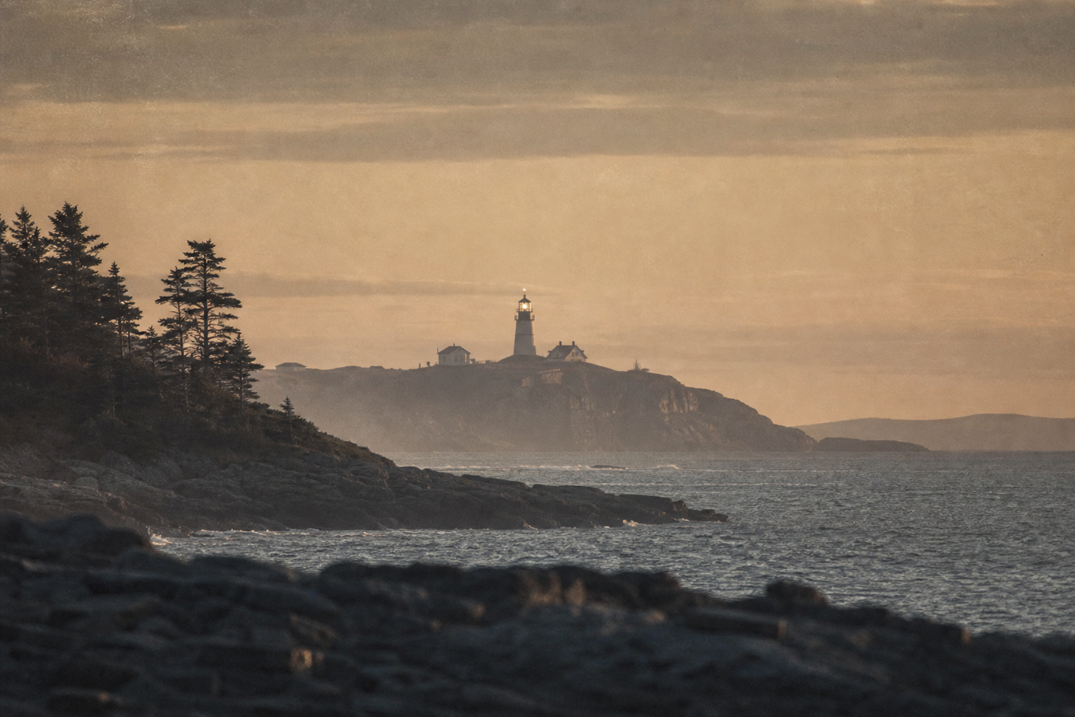 Distant lighthouse beacon silhouette at dusk across the headland