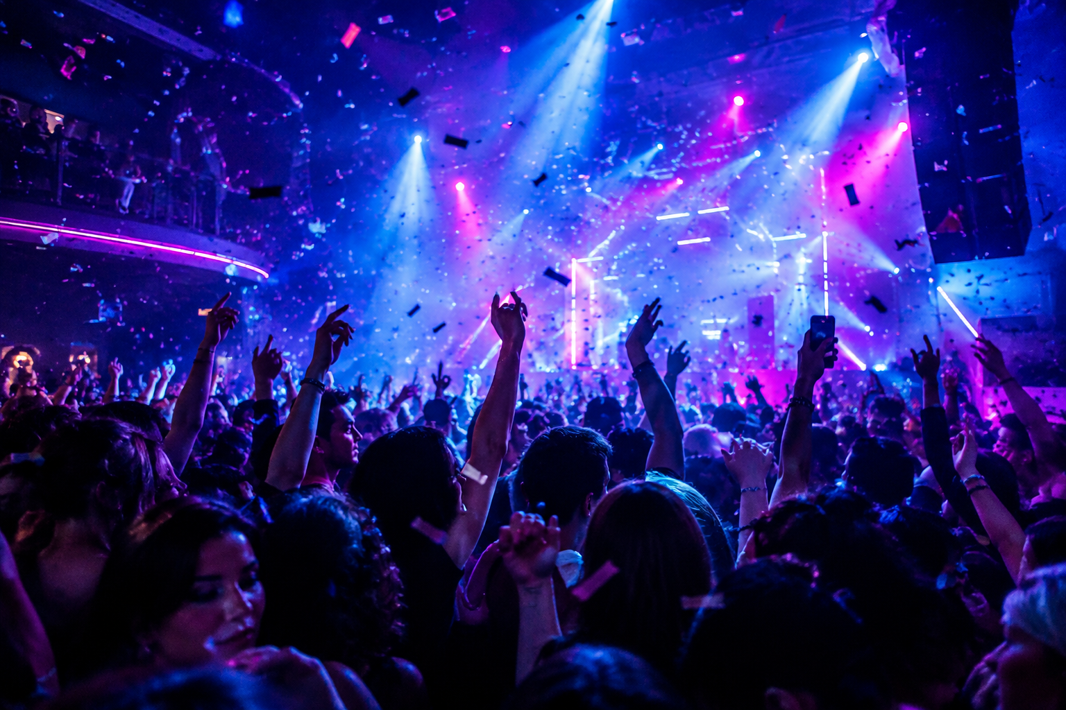 High-energy nightlife crowd with raised hands, dense dance floor, and dramatic club lighting