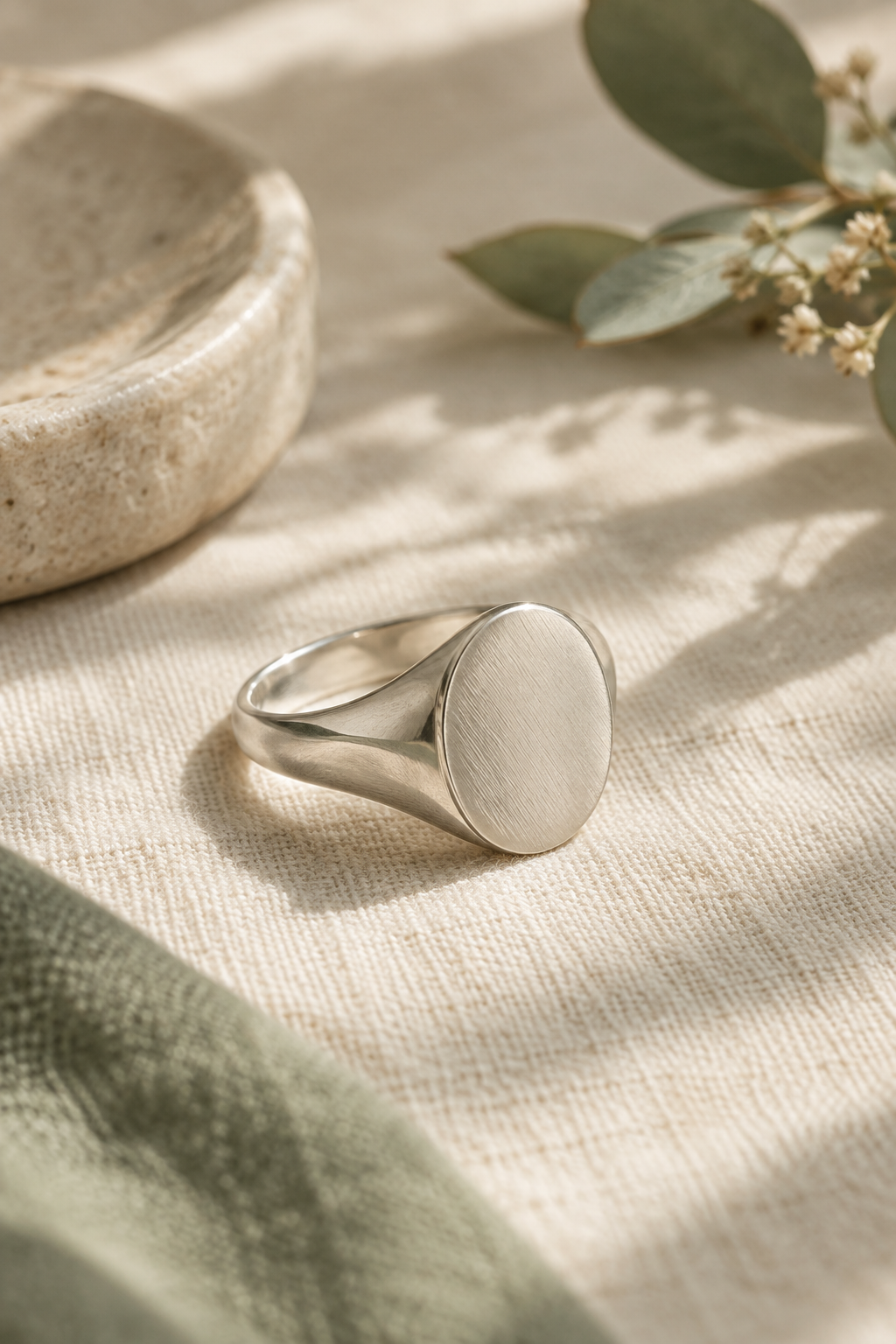 Handmade oval silver signet ring with a softly brushed face on warm linen