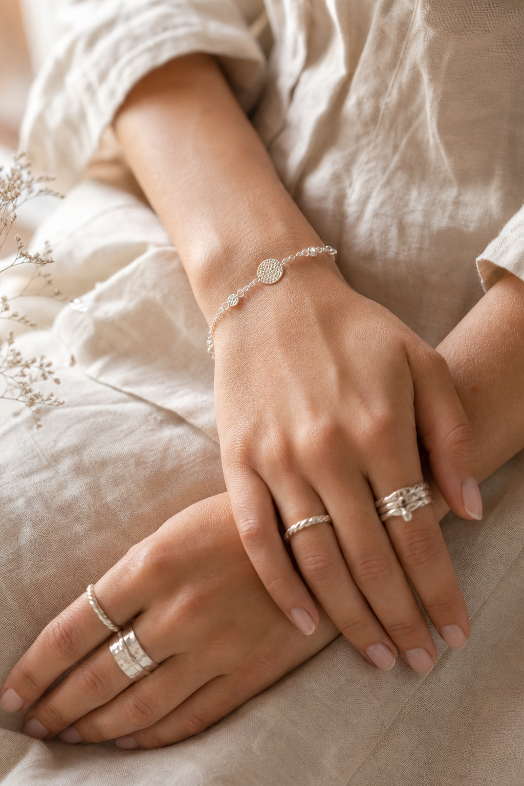 Close-up artisan jewelry lifestyle portrait with hands, silver rings, woven texture, and soft natural styling