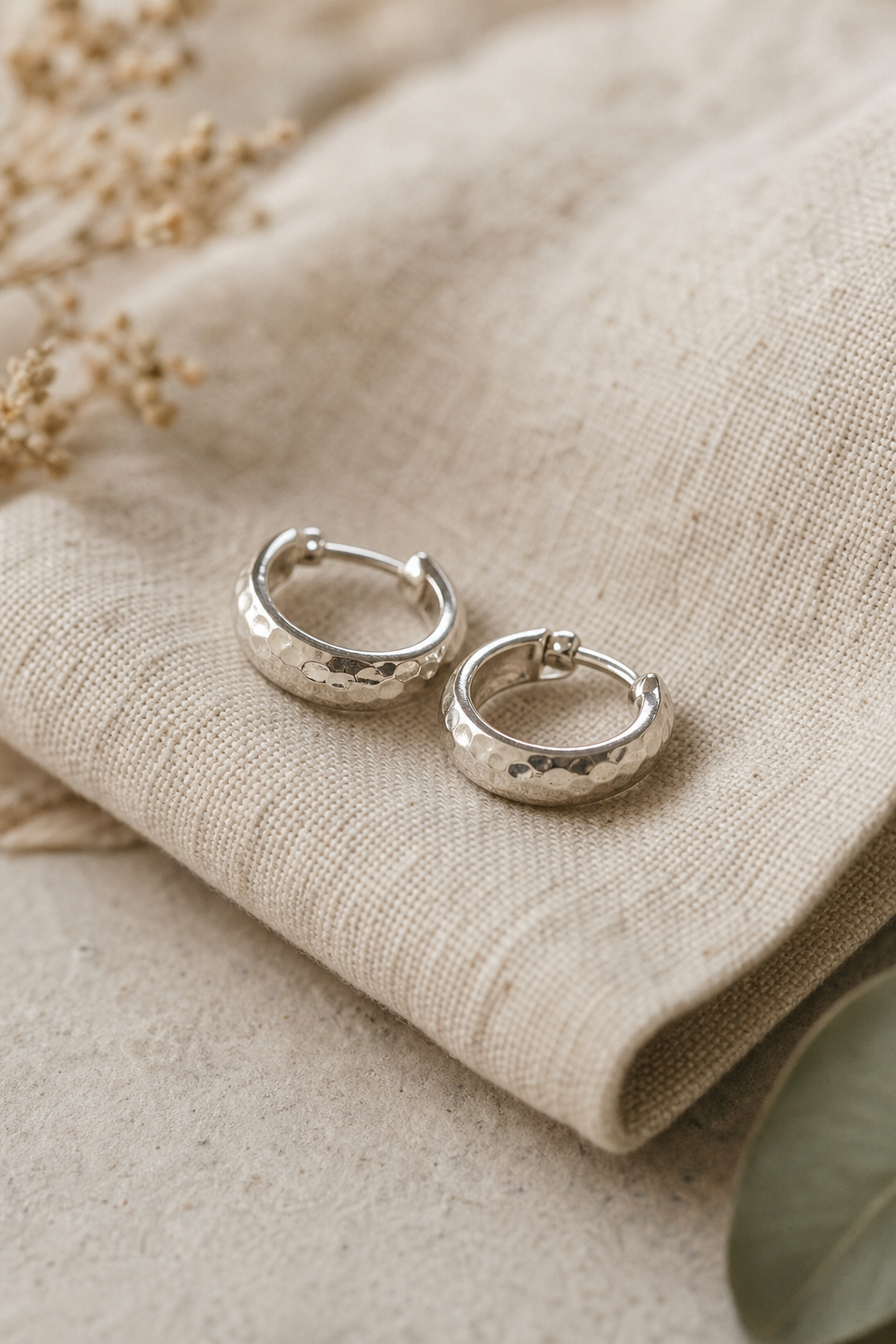 Pair of hammered silver hoop earrings resting on natural linen fabric