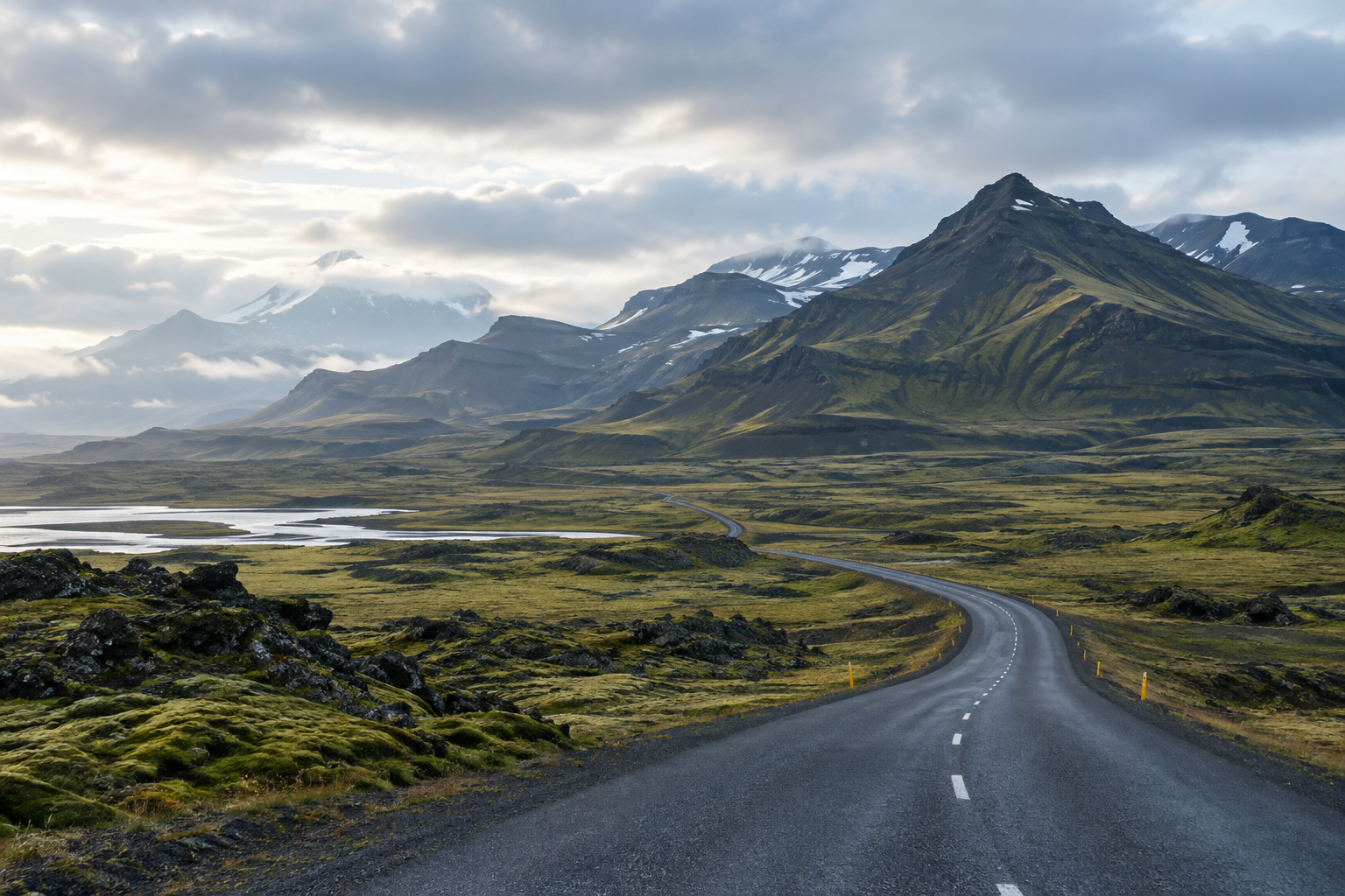 A cinematic view across Icelandic highlands, with a winding road, distant mountains, and soft northern light