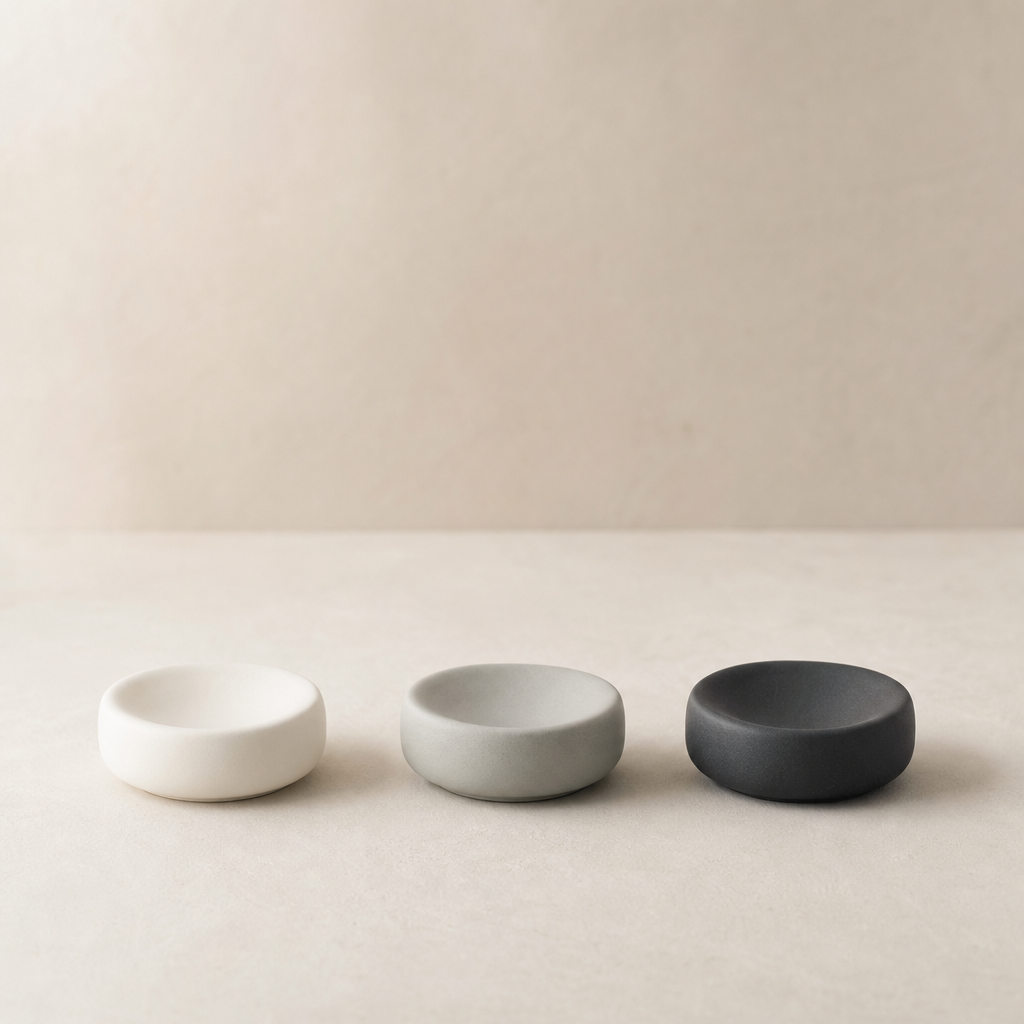 Three small matte porcelain cup rests in off-white, mist gray, and charcoal arranged in a row