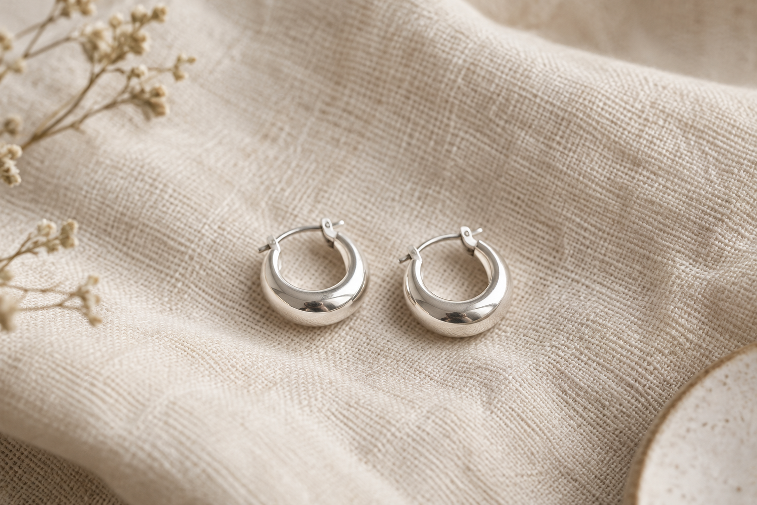 Pair of small sculptural sterling silver hoop earrings with a softly polished finish on ivory cloth