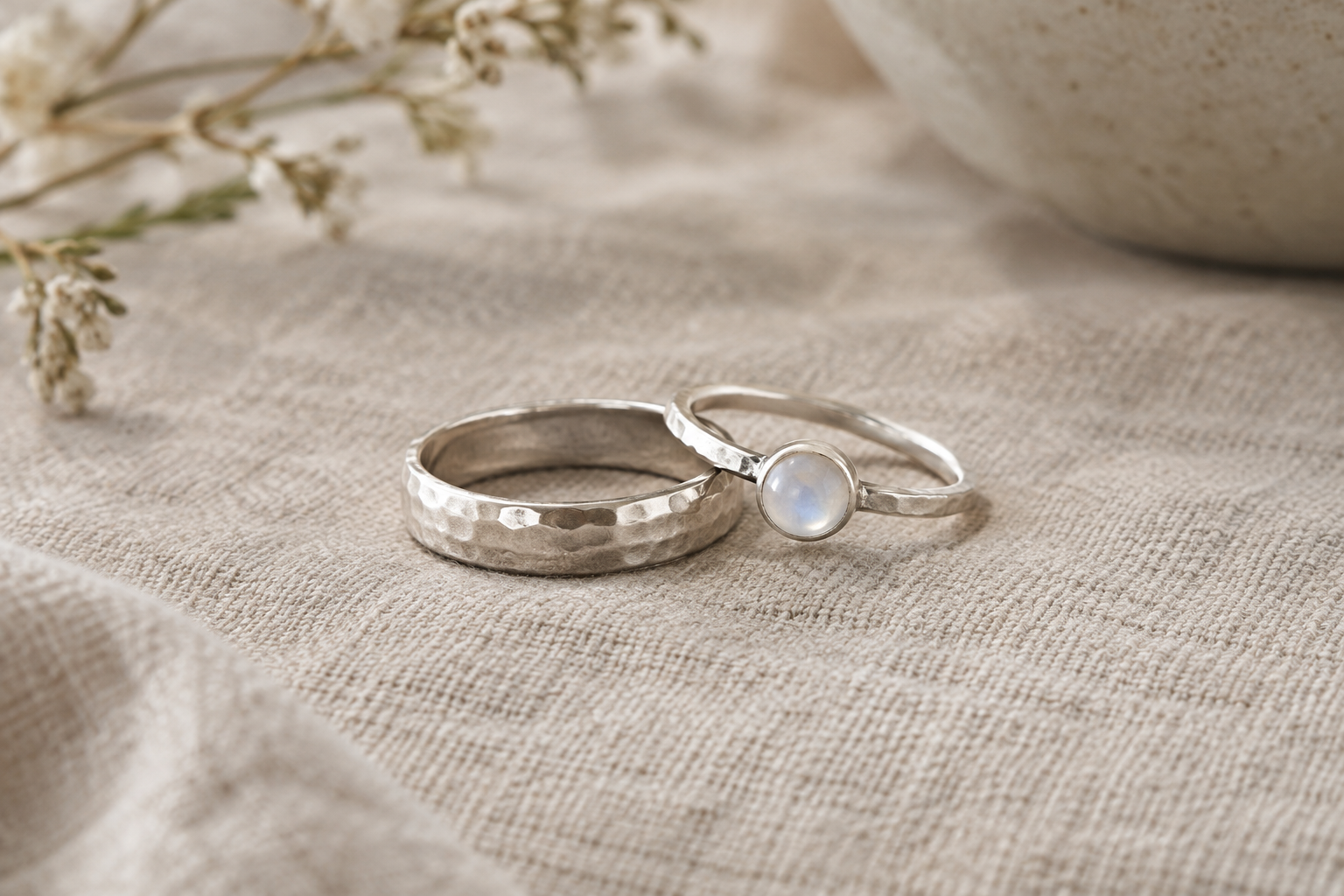 Handcrafted sterling silver rings, including a softly hammered band and a delicate moonstone ring, arranged on natural linen