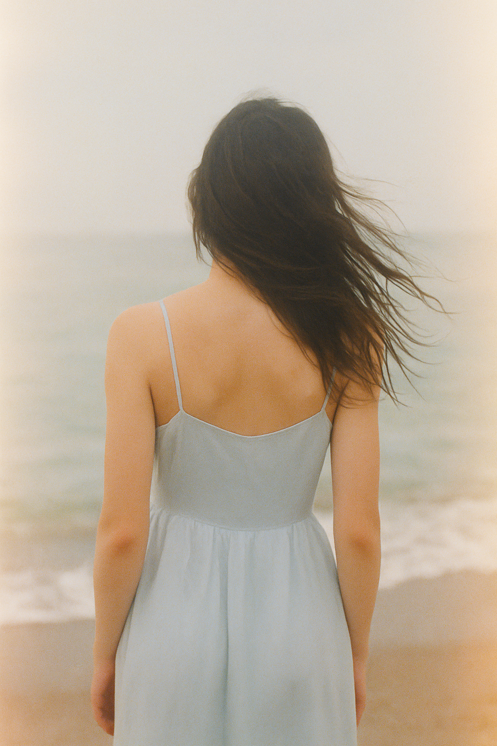 Hazy pastel film photograph of a woman by the sea with windswept hair