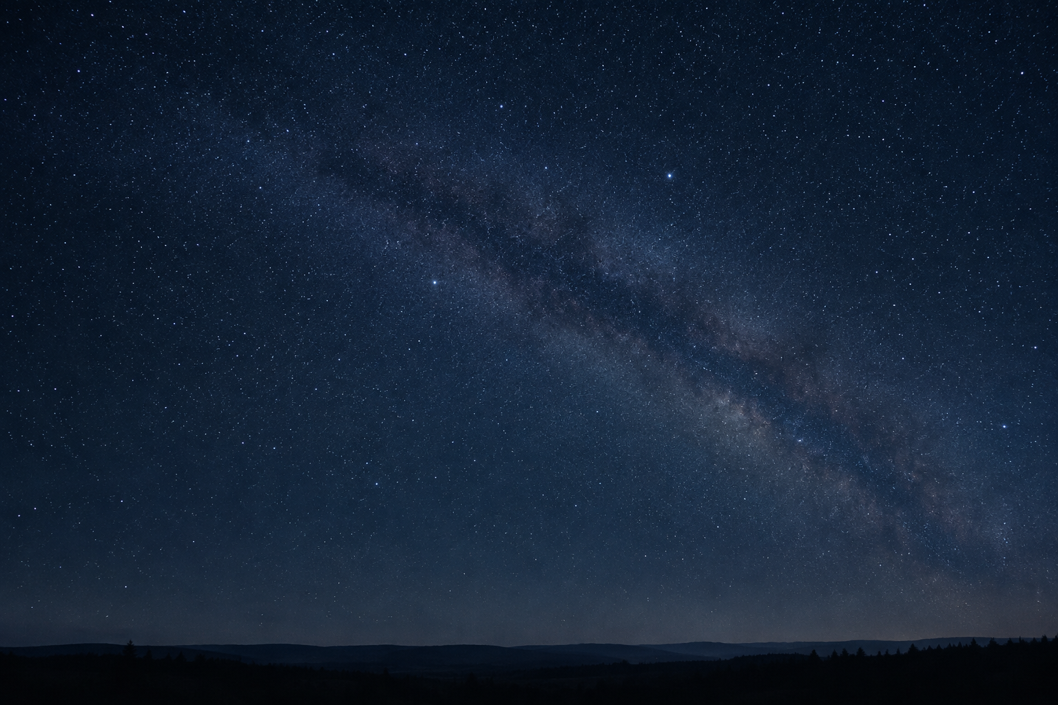 Long-exposure night sky filled with fine stars and a faint Milky Way band over a low dark horizon