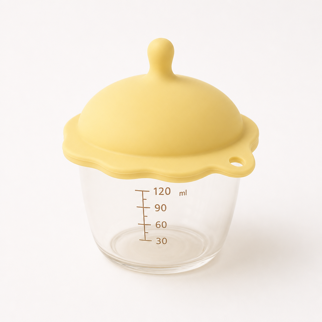 Small baby food cup with soft silicone lid in pastel yellow, photographed on light background