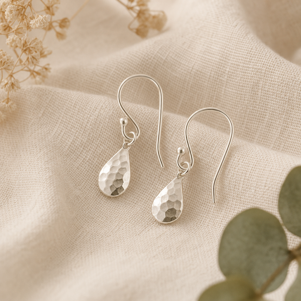 Pair of delicate sterling silver drop earrings resting on soft neutral fabric
