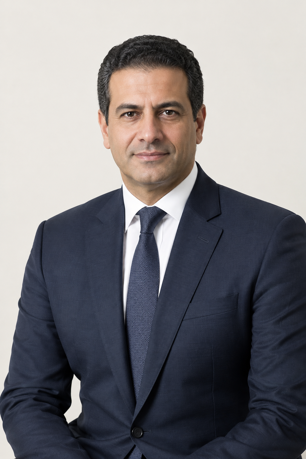 Formal studio portrait of Haitham L. Husseiny in a dark tailored suit, calm expression, neutral off-white background