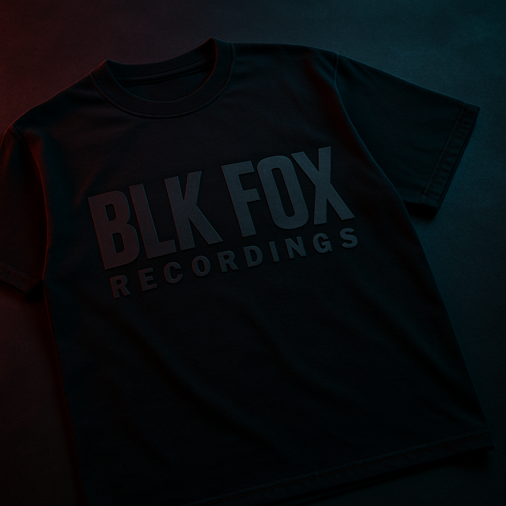 Black heavyweight festival t-shirt laid flat, bold tonal logo across the chest, moody studio lighting