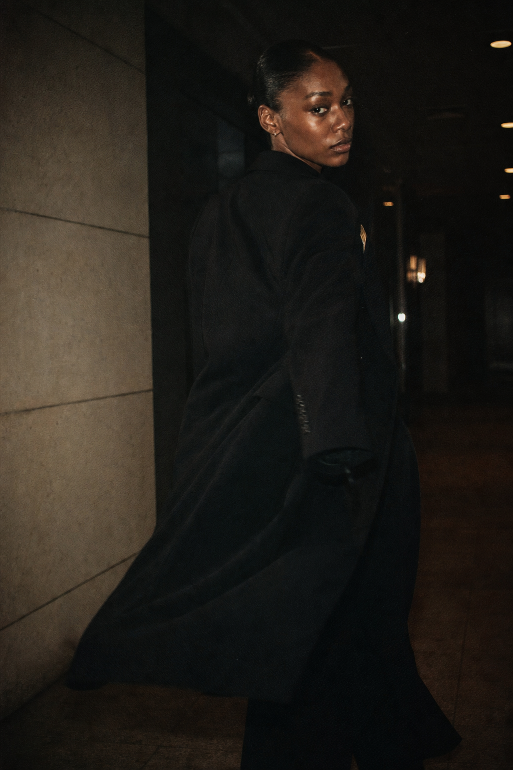 35mm fashion portrait with subtle motion blur as model turns in a dark hallway