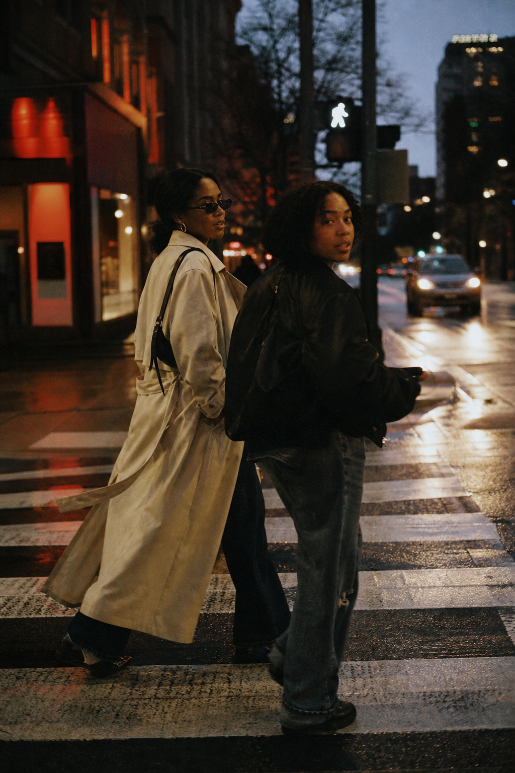 candid 35mm lifestyle frame of two friends crossing a city street at dusk