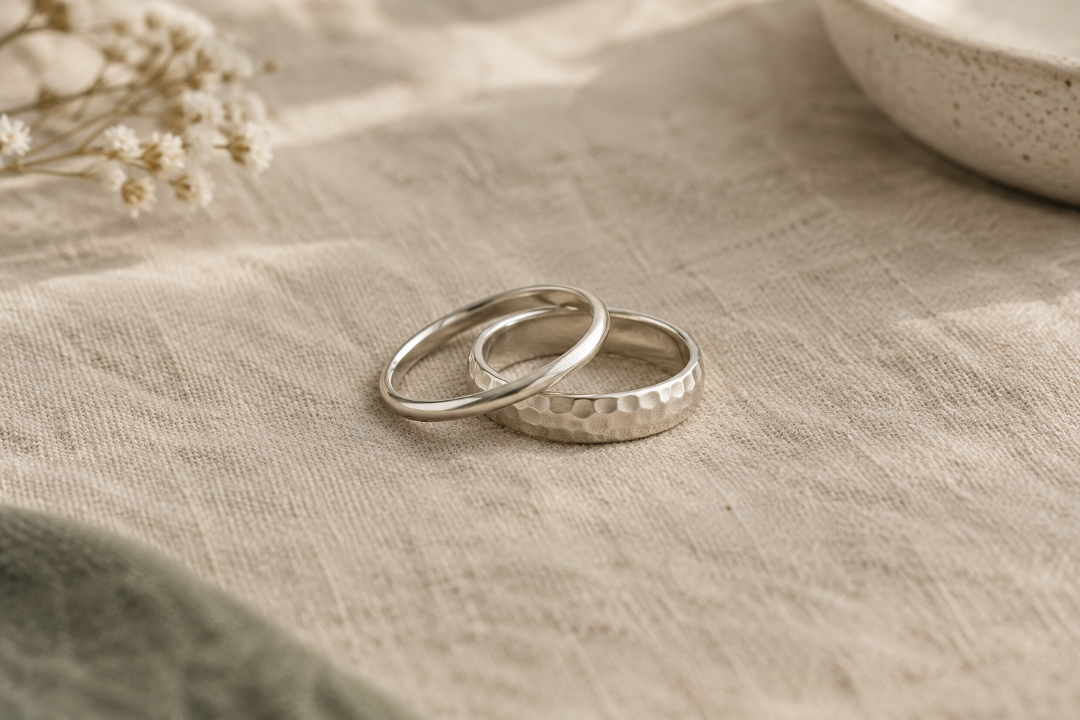 Two handcrafted silver stacking rings with gently hammered surfaces on natural linen