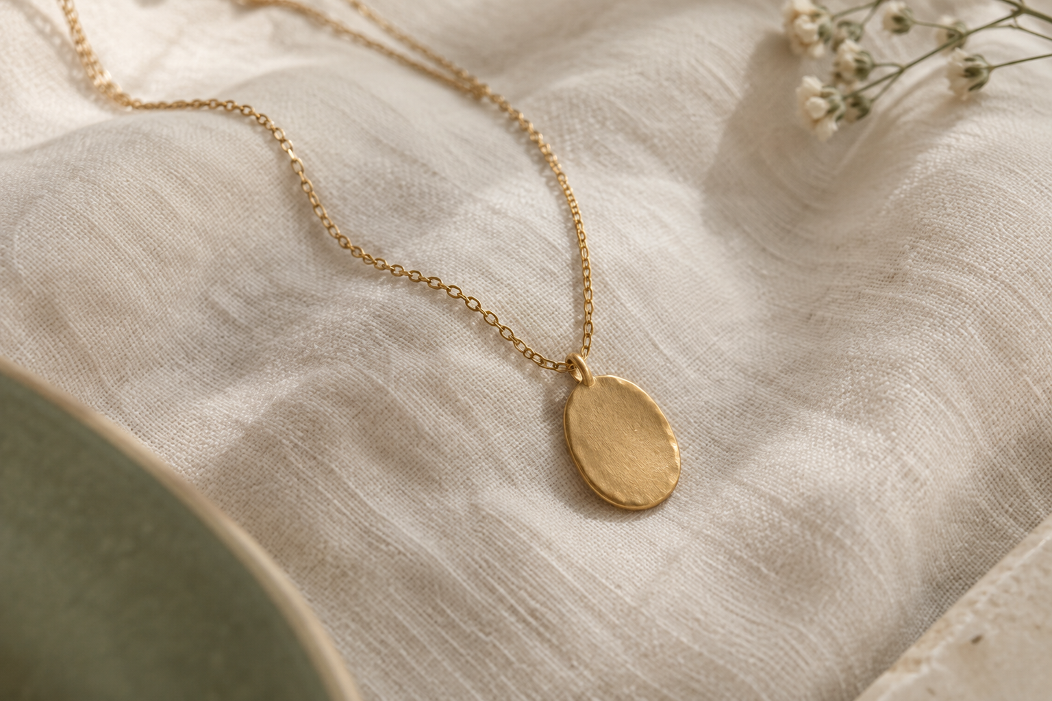 An oval brushed-gold pendant and delicate chain on cream cotton