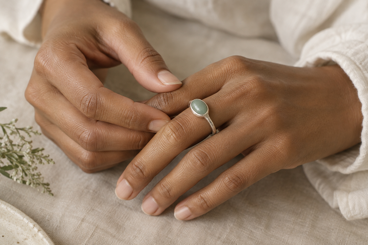Hands gently styling a silver ring set with a pale green oval stone