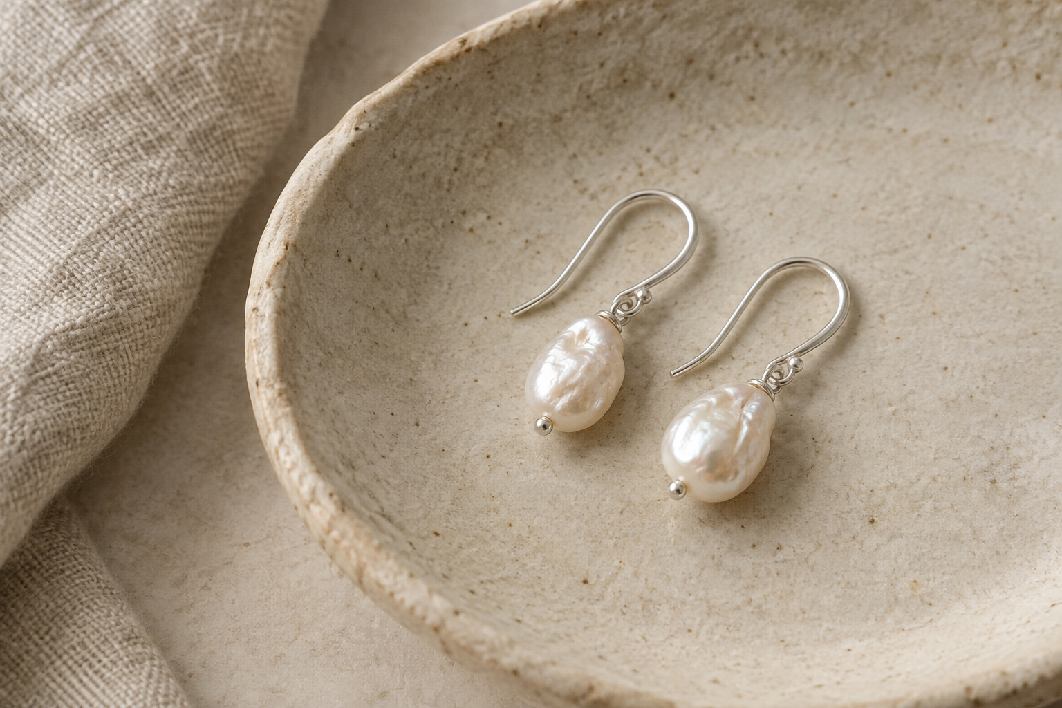 Small freshwater pearl drop earrings with silver hooks on a ceramic dish