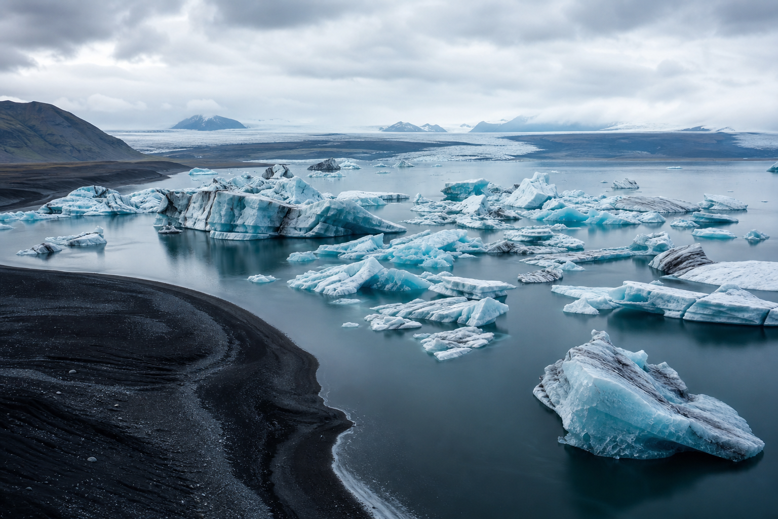 Aerial view of an Icelandic glacial lagoon with pale blue icebergs and black volcanic sand beach
