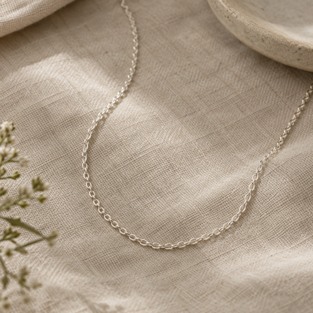 Delicate sterling-silver trace chain arranged in a loose curve on textured neutral fabric