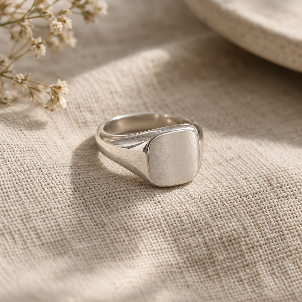 Hand-finished silver signet ring with a softly squared face on warm linen