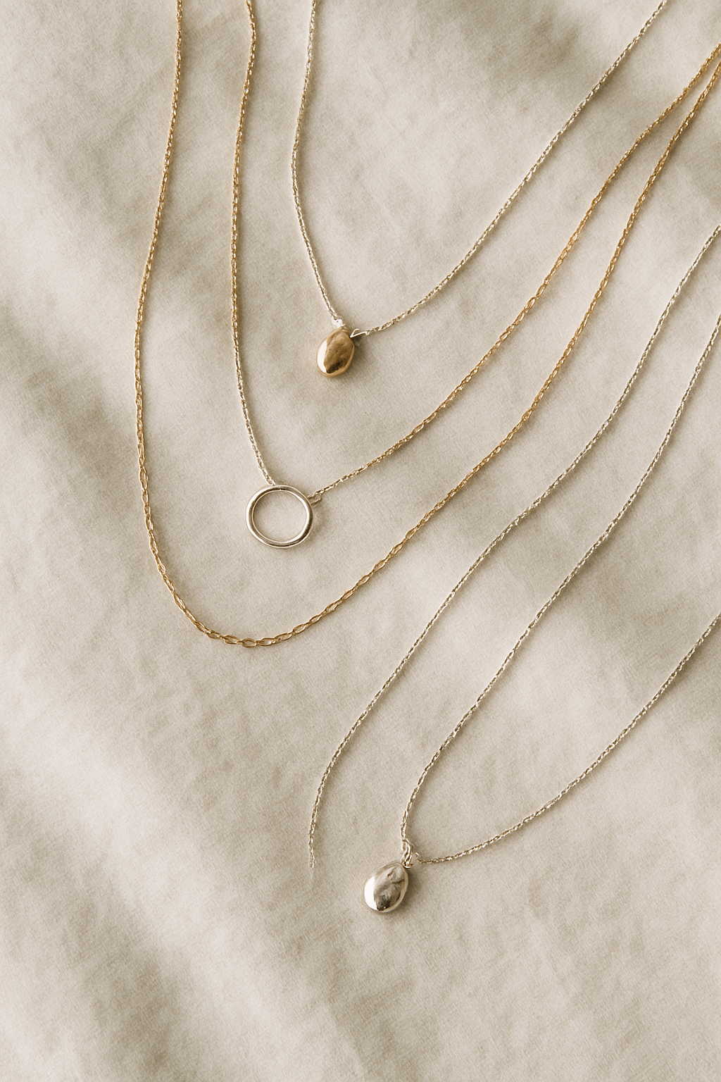 Delicate layered necklaces arranged on soft linen fabric