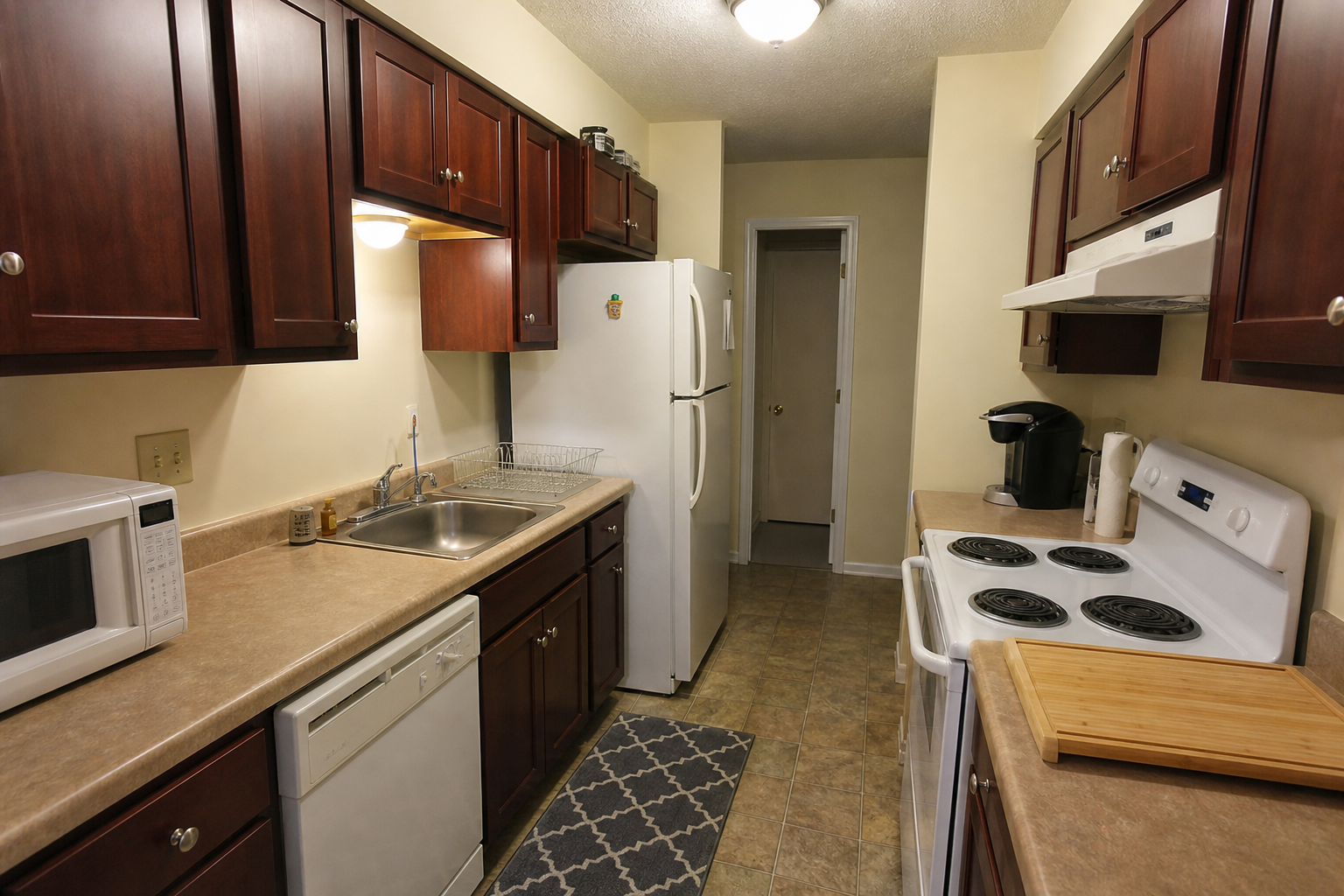 Before photo of a narrow kitchen with dark cabinets, limited counter space, and older appliances