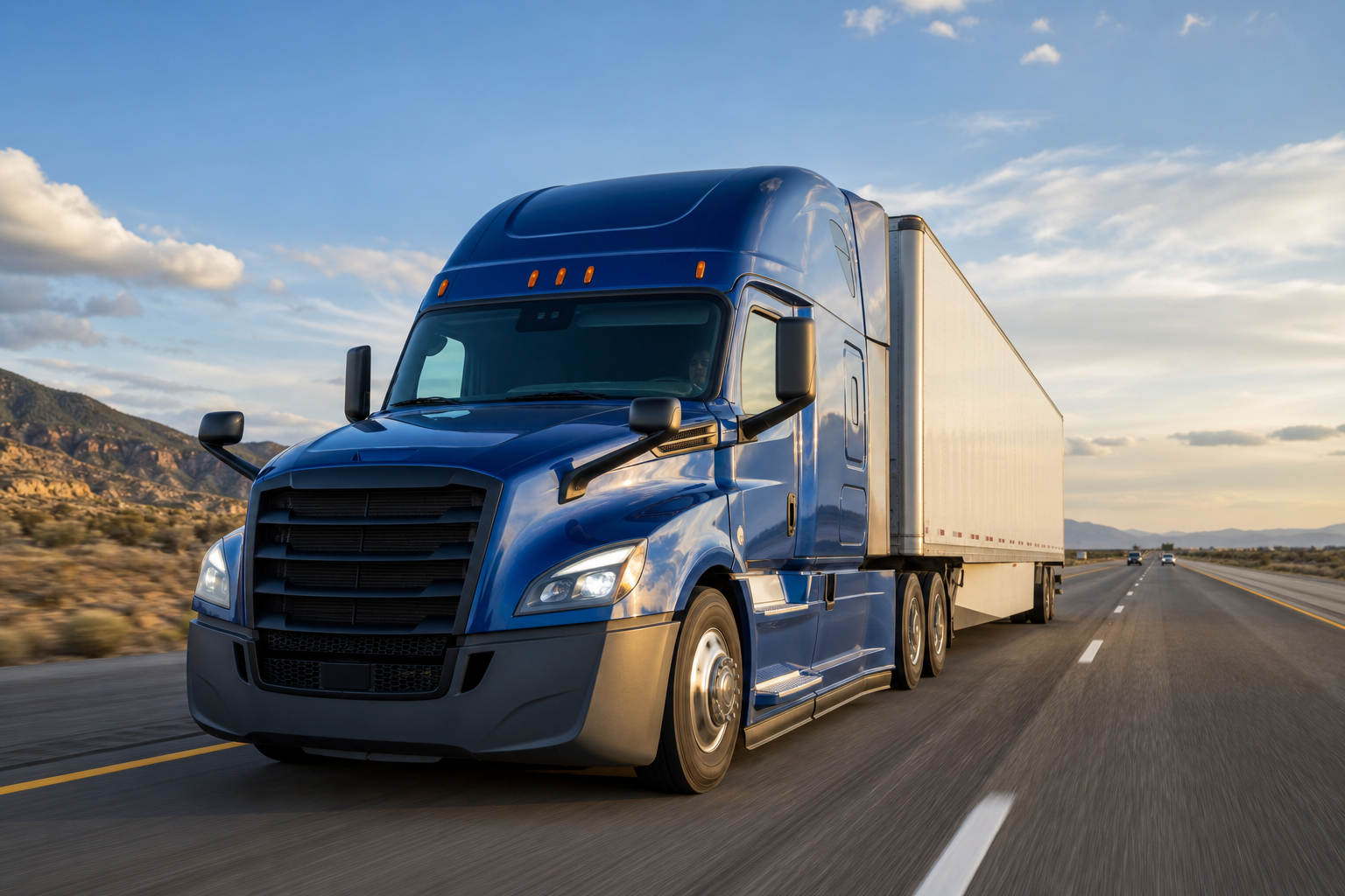 Blue semi-truck hauling a white freight trailer on a U.S. highway at golden hour