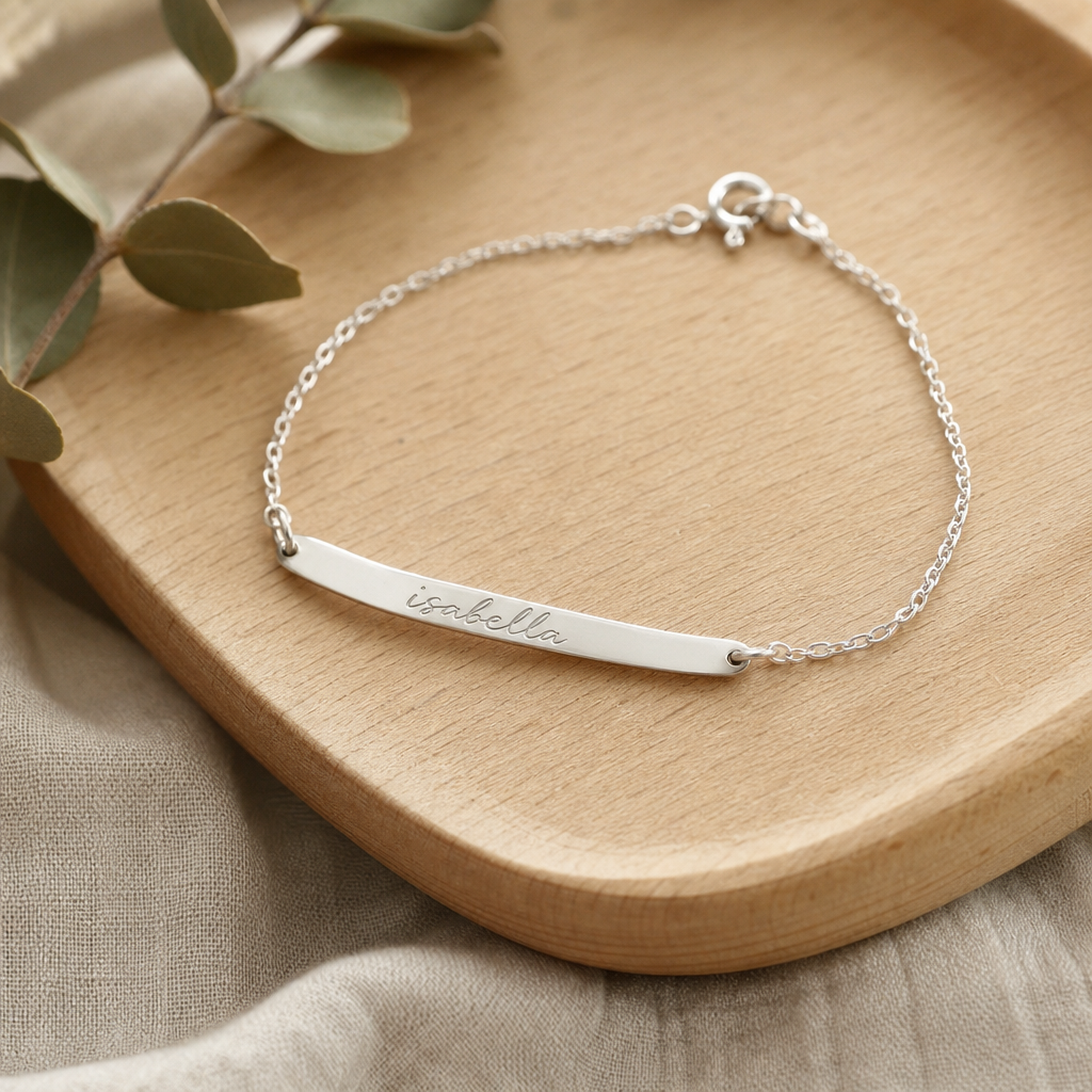 Thin silver bracelet with a hand-engraved name script laid on a wooden jewelry tray