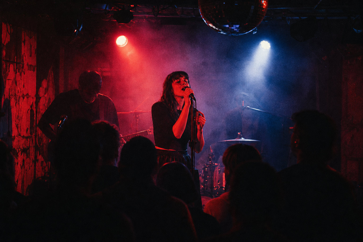 Live music performance frame with vocalist under red and blue stage lights, haze in the air, and grainy cinematic texture