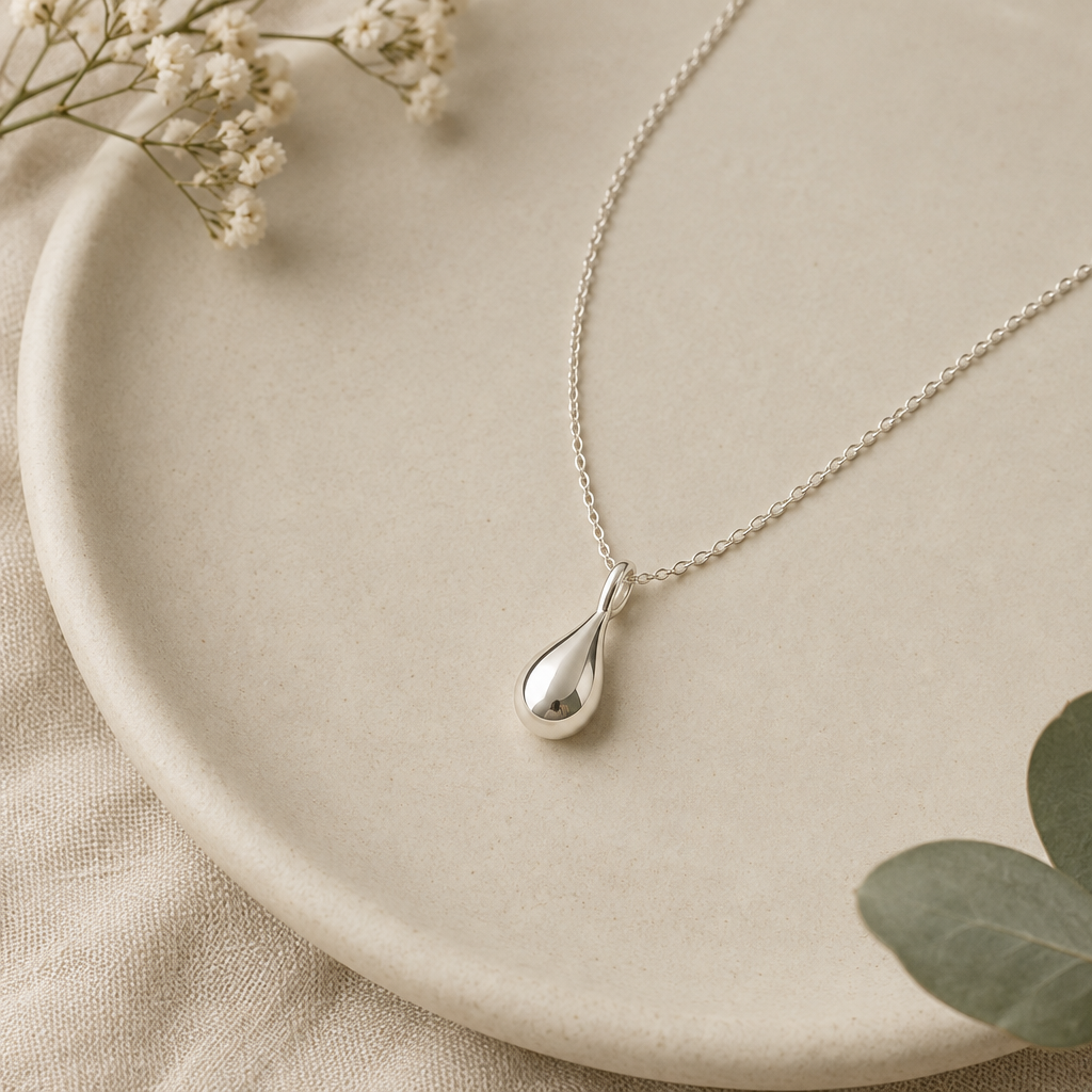 Delicate silver dewdrop pendant necklace on a soft neutral surface