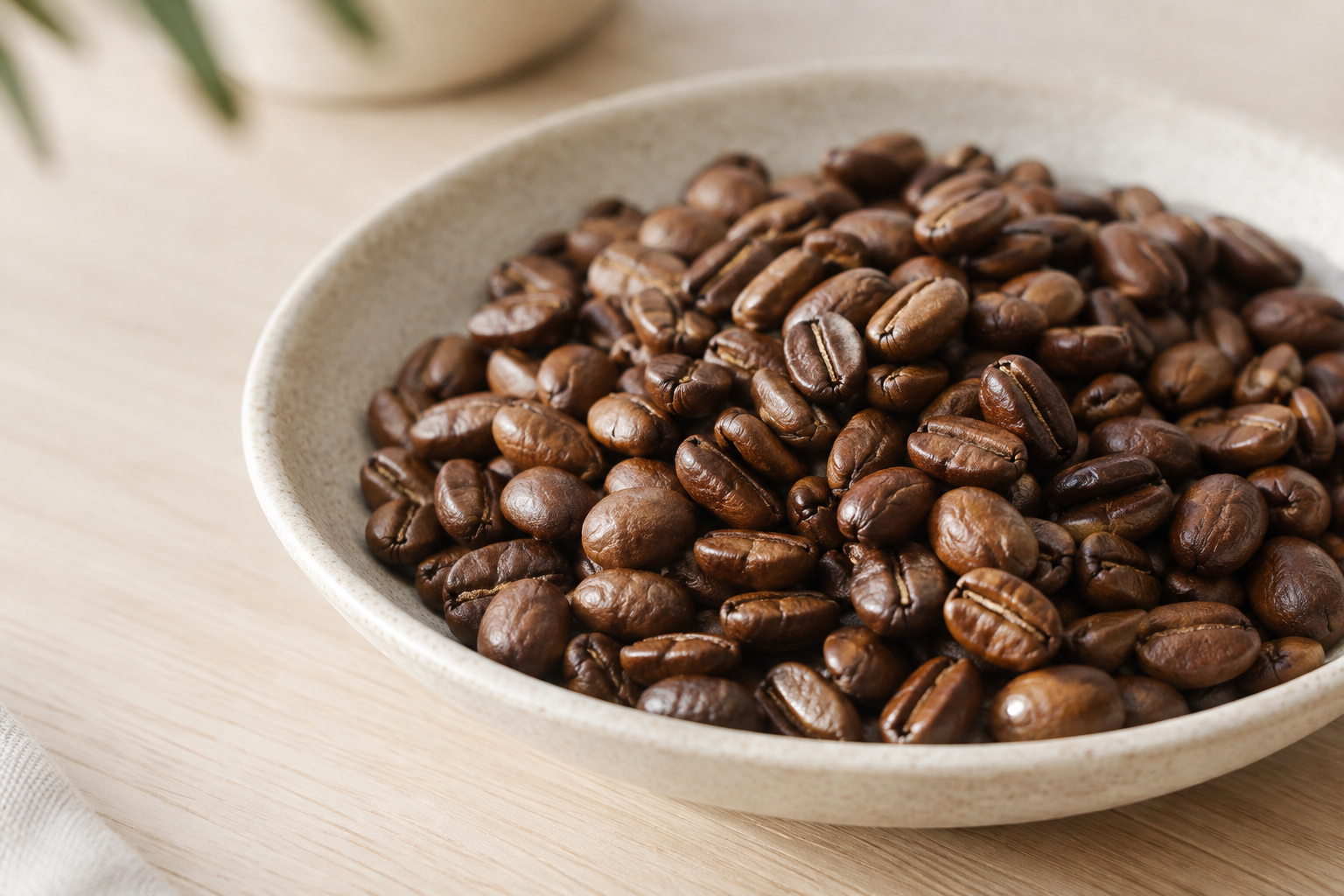 Textural close-up of glossy roasted coffee beans in a pale stoneware dish