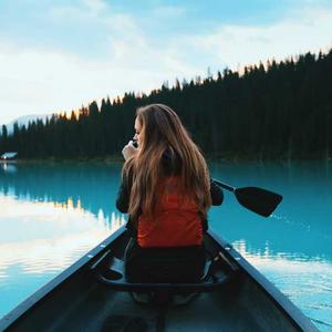 Person in a red jacket paddling a canoe on calm water