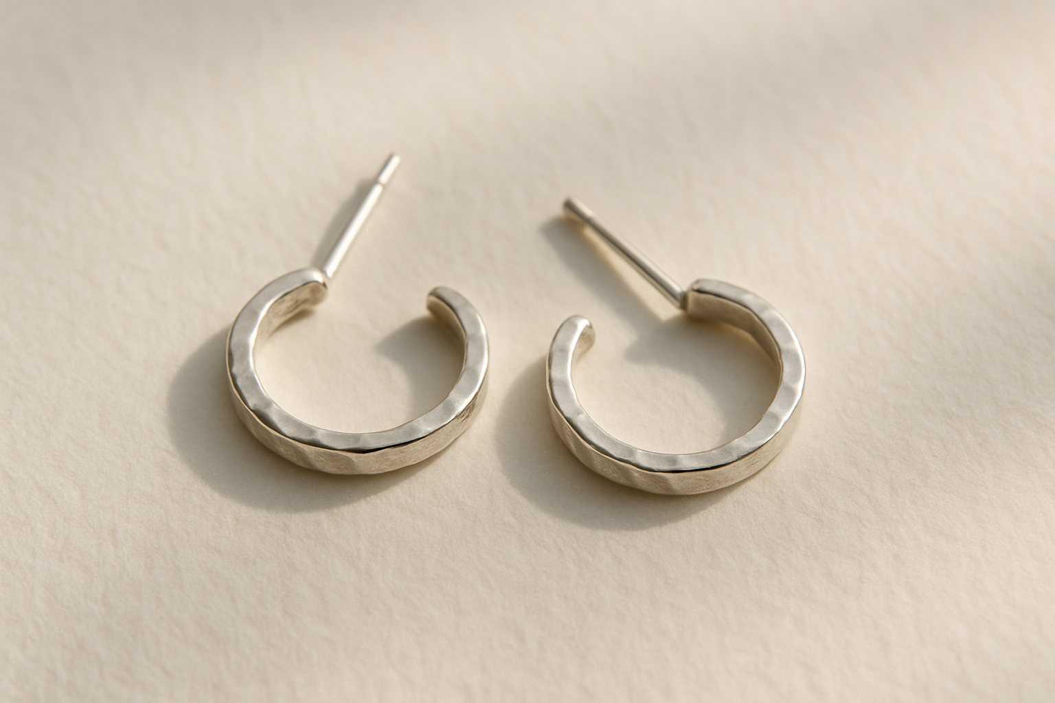 Pair of small handmade hammered silver hoop earrings on a soft cream paper background