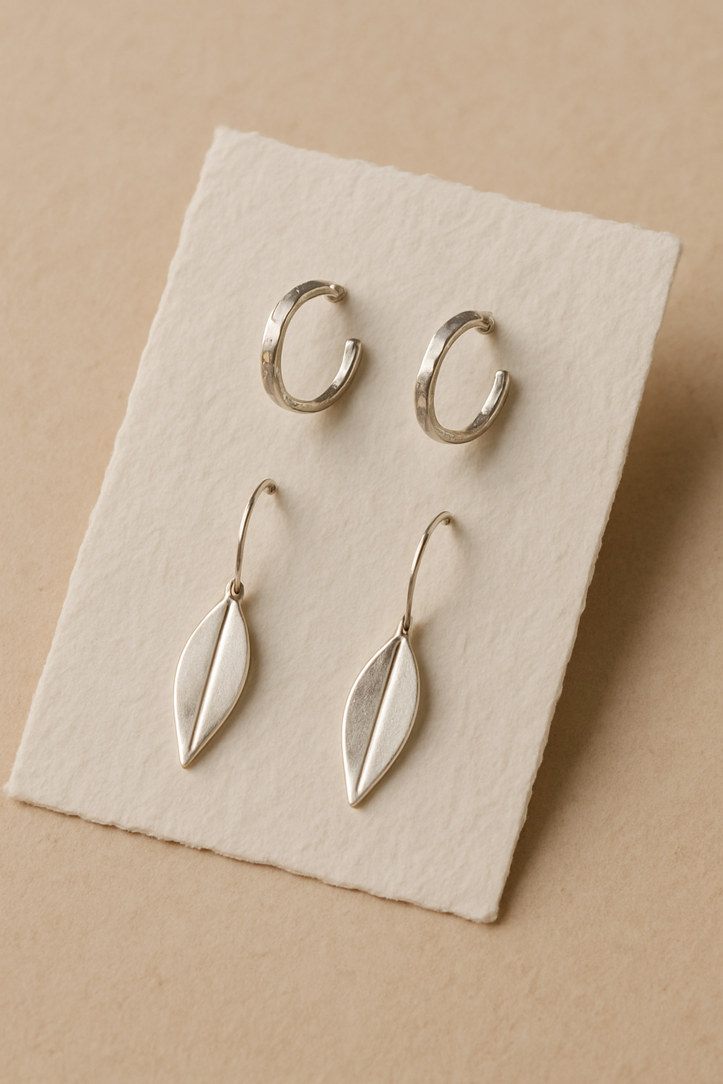 Small handmade silver hoop and drop earrings on a textured paper card
