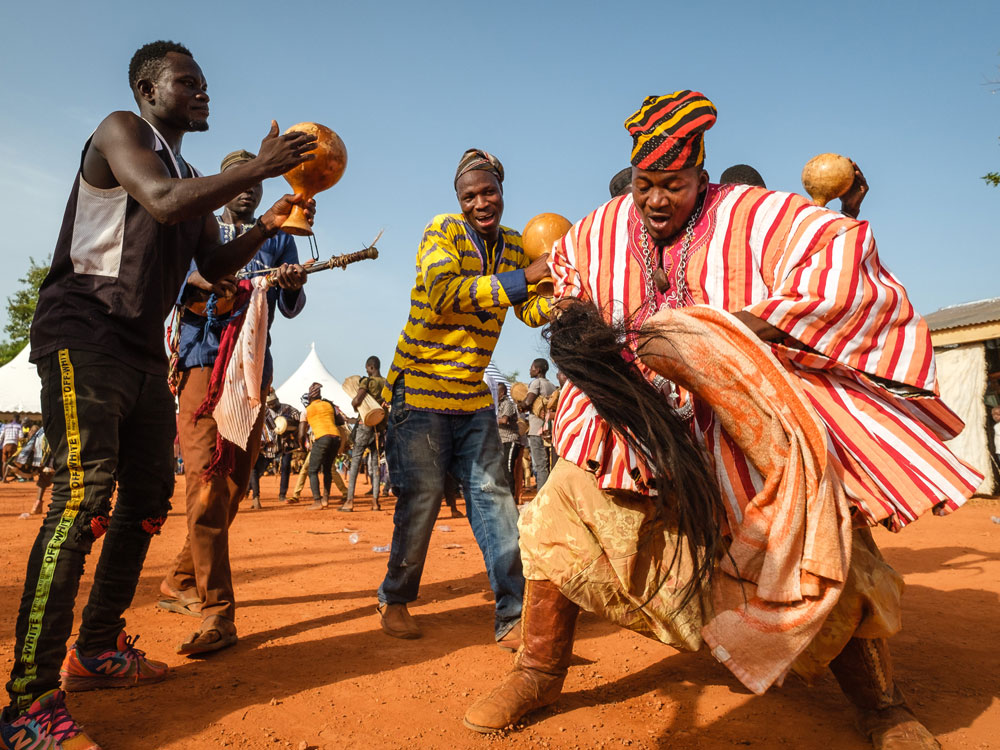 Outdoor cultural dance performance on red earth with musicians and a lead dancer in striped traditional attire