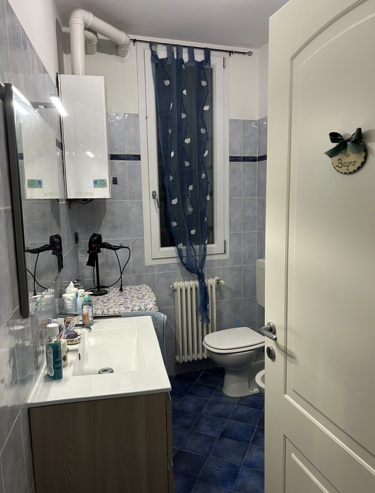 Bagno con rivestimenti nei toni del blu, lavabo con specchio, finestra centrale e sanitari bianchi