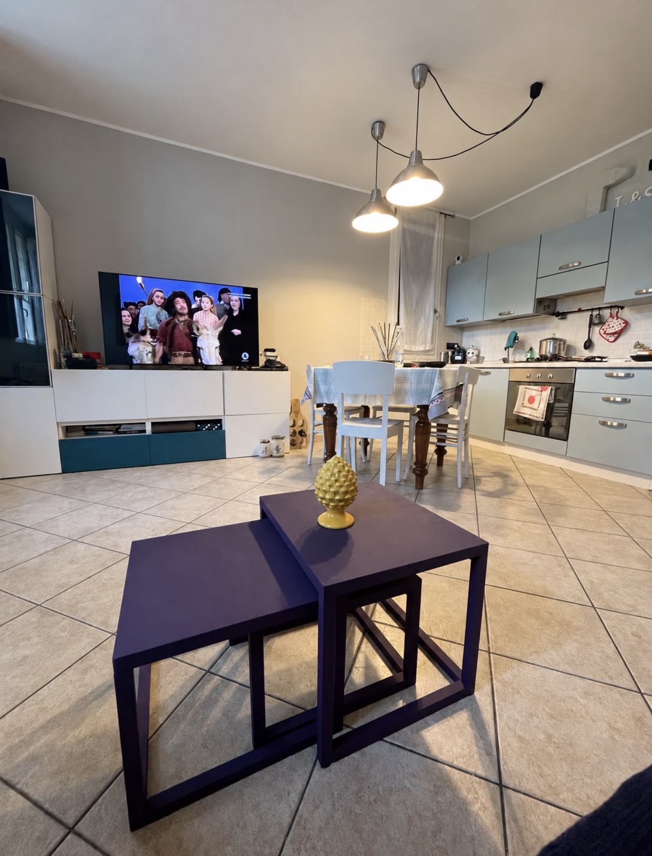 Cucina luminosa open space con tavolo da pranzo, sedie bianche, mobili chiari e zona living sullo sfondo
