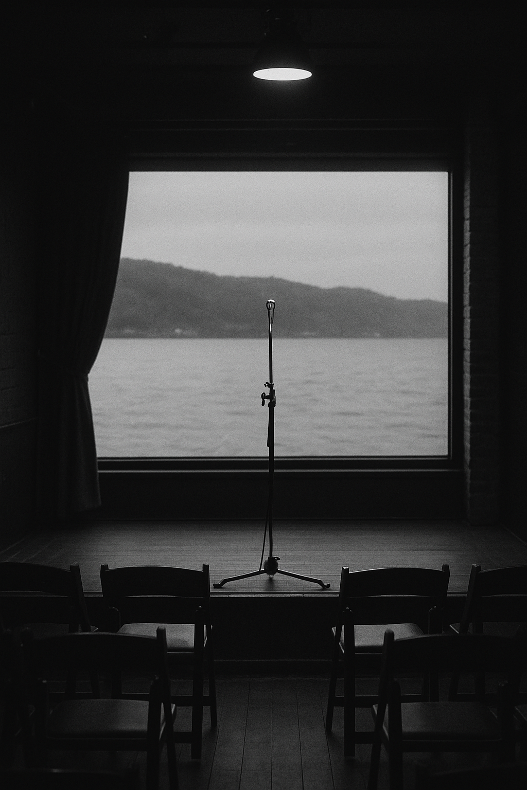 Monochrome photo of a small Hudson River venue stage with empty chairs and a microphone stand