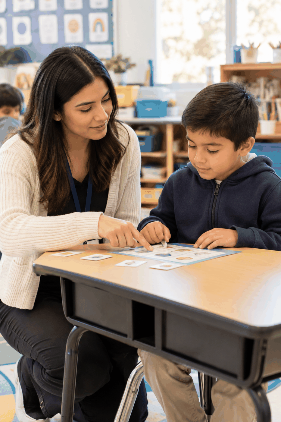 An educator and caregiver supporting an elementary student during a calm one-on-one learning activity in a bright Southern California classroom